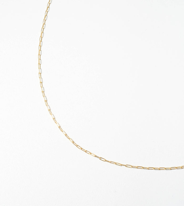 The Adelene Paperclip Chain by LLUME Jewelry, featuring small rectangular gold-plated links, is displayed in a graceful curve against a plain white background.