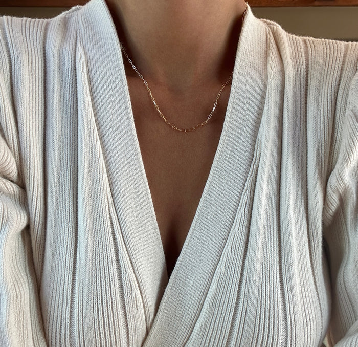 A person wearing a cream ribbed wrap sweater and the LLUME Jewelry Adelene Paperclip Chain necklace, photographed from the shoulders to just below the chin.
