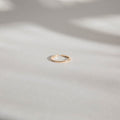 An LLUME Jewelry Adjustable Stacking Ring in 14k gold-fill rests on a smooth, light-toned surface, with gentle, blurred shadows in the background.