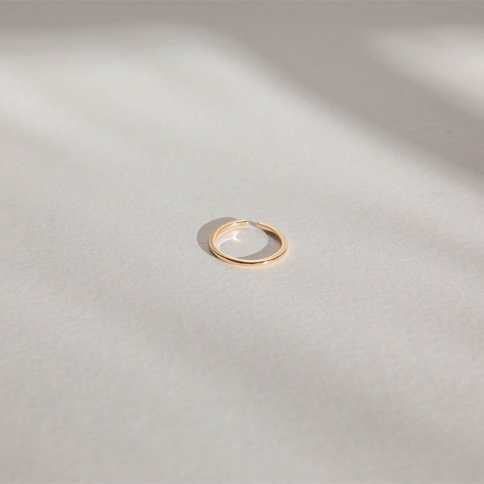 The LLUME Jewelry Adjustable Stacking Ring in 14k gold-fill rests on a light, textured surface, with soft shadows and diffused sunlight for a minimal, serene look.