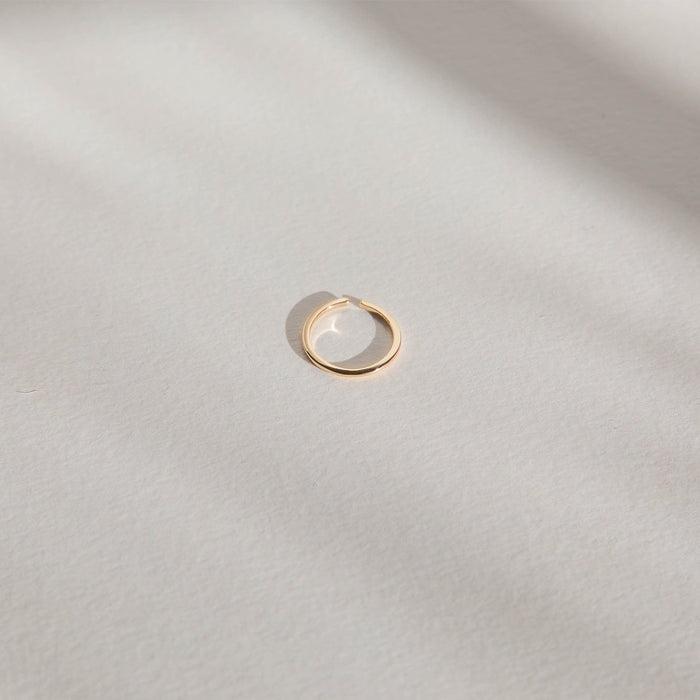 An LLUME Jewelry Adjustable Stacking Ring in 14k gold-filled rests on a textured, light surface with soft shadows, highlighting its minimalistic and elegant design.
