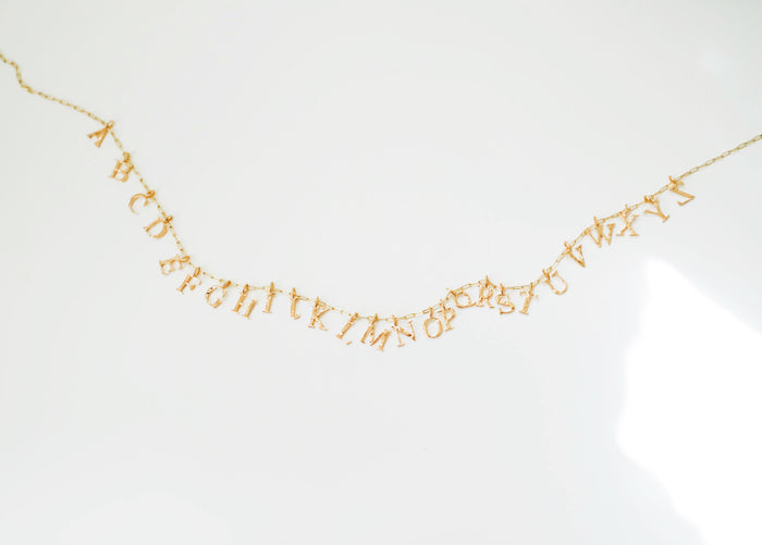 The LLUME Jewelry Alphabet Charm Necklace features gold alphabet charms in English order, showcased on a plain white background—a charming and personalized jewelry piece.