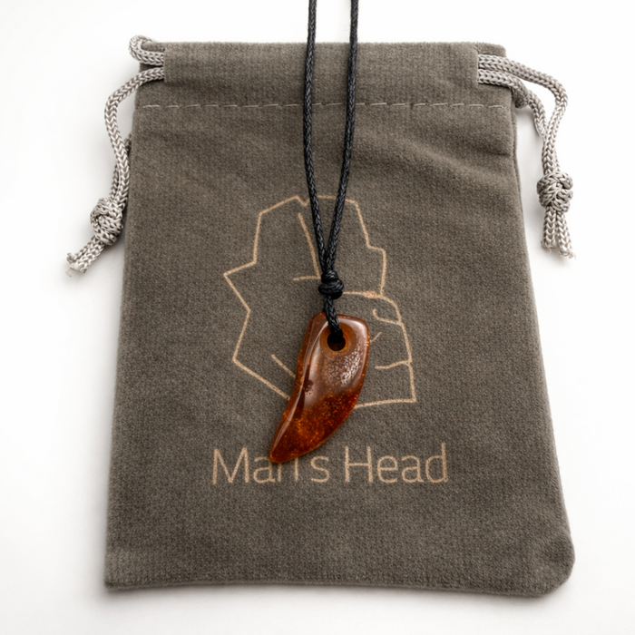 Natural amber tooth pendant on black cord displayed on a soft pouch with logo on a clean white background