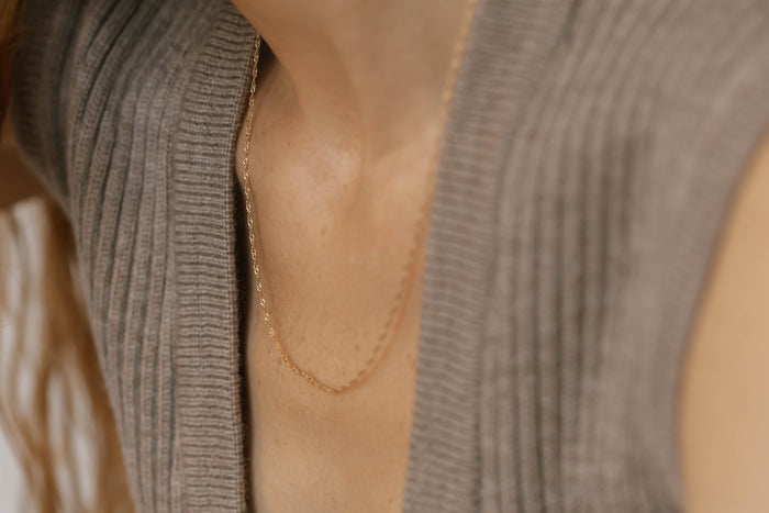 A close-up of a person wearing a ribbed taupe sleeveless sweater and the LLUME Jewelry Angel Twist Necklace, an elegant gold plated piece, highlighting their neck and upper chest.