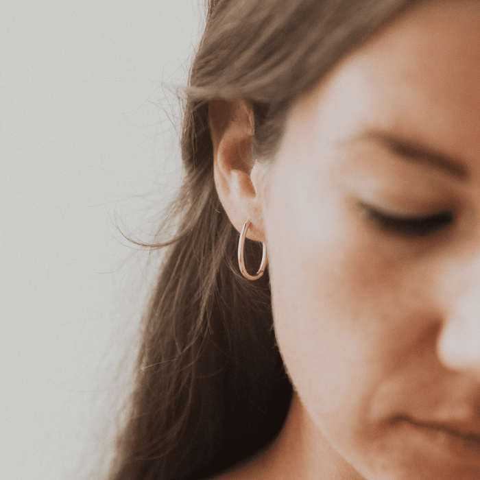 Close-up of a woman's ear wearing LLUME Jewelry's Athena Oval Hoops, softly lit with hints of her brown hair and blurred facial features.