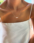 A person wearing a white satin camisole and the Avery Pearl Necklace by LLUME Jewelry, a dainty piece adorned with four small freshwater pearls, shown from shoulders to chest in natural light.
