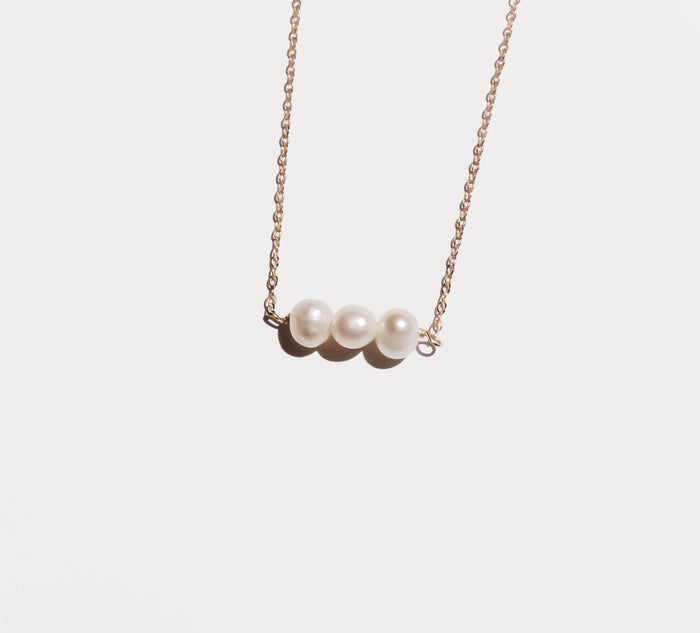 The Avery Pearl Necklace by LLUME Jewelry features a delicate gold chain with three freshwater pearls in a row, elegantly presented on a plain white background.