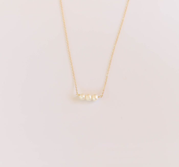 The Avery Pearl Necklace by LLUME Jewelry is a delicate gold necklace featuring three small freshwater pearls in a row, showcased on a plain white background.