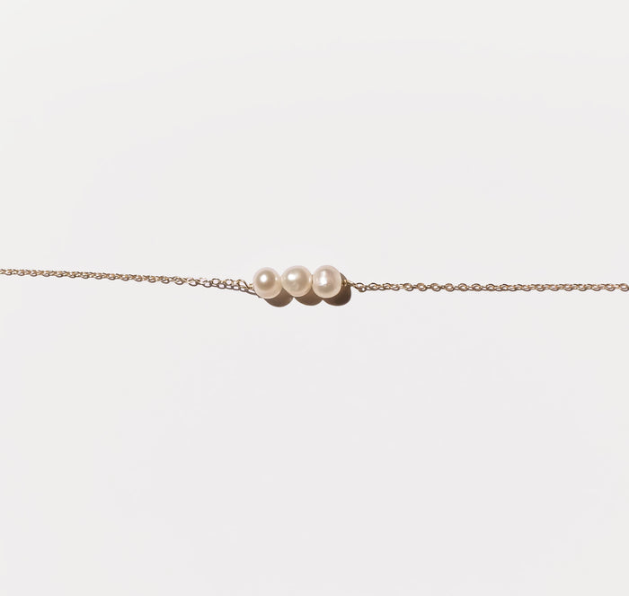 The Avery Pearl Necklace by LLUME Jewelry showcases a delicate gold chain with three freshwater pearls in a row, elegantly displayed against a plain white background.