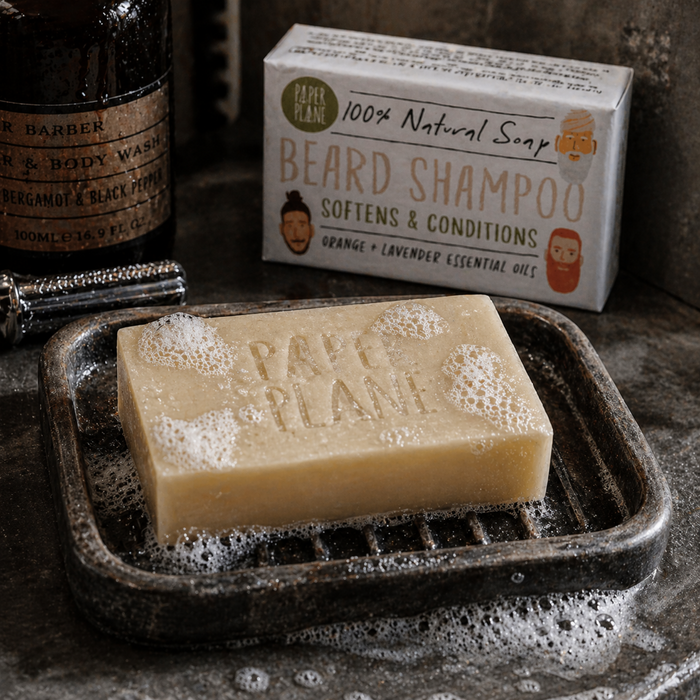 Paper Plane beard shampoo soap bar with lather in dark soap dish and boxed bar in rustic masculine bathroom setting
