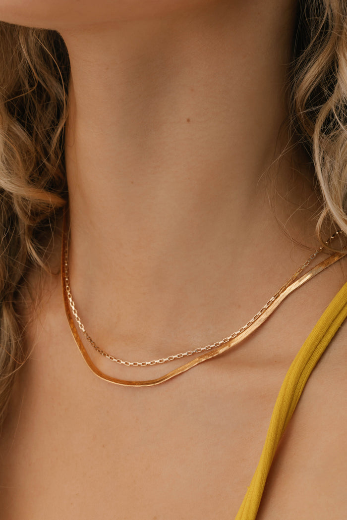 Close-up of a woman’s neck adorned with LLUME Jewelry’s Beverly Set—timeless gold layered chains. Her wavy blonde hair and yellow thin-strap top evoke understated elegance.