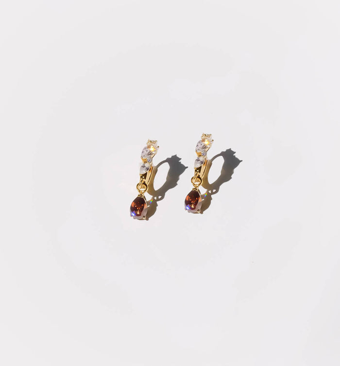 The Blair Earrings by LLUME Jewelry showcase gold drops, clear stones on top, and small oval brown gemstones below—an elegant accessory set against a plain white background.