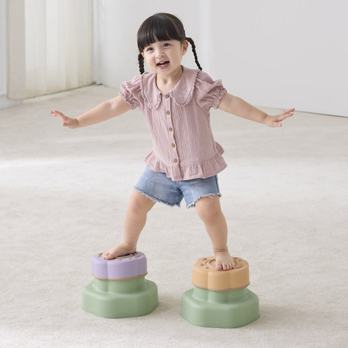 Child standing on two colorful step stools in a room with a white floor and light-colored walls.