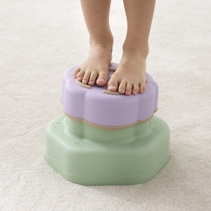 Child's feet on a two-tone step stool with purple top and green bottom on a light carpet.
