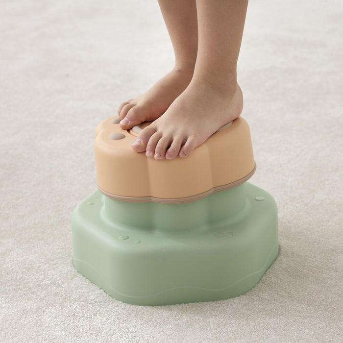 Step stool with a child's feet on it, on a light carpeted floor.