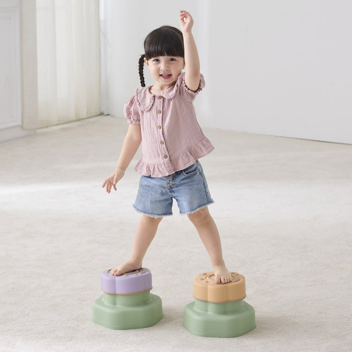 Child standing on two colorful step stools in a minimalistic room.