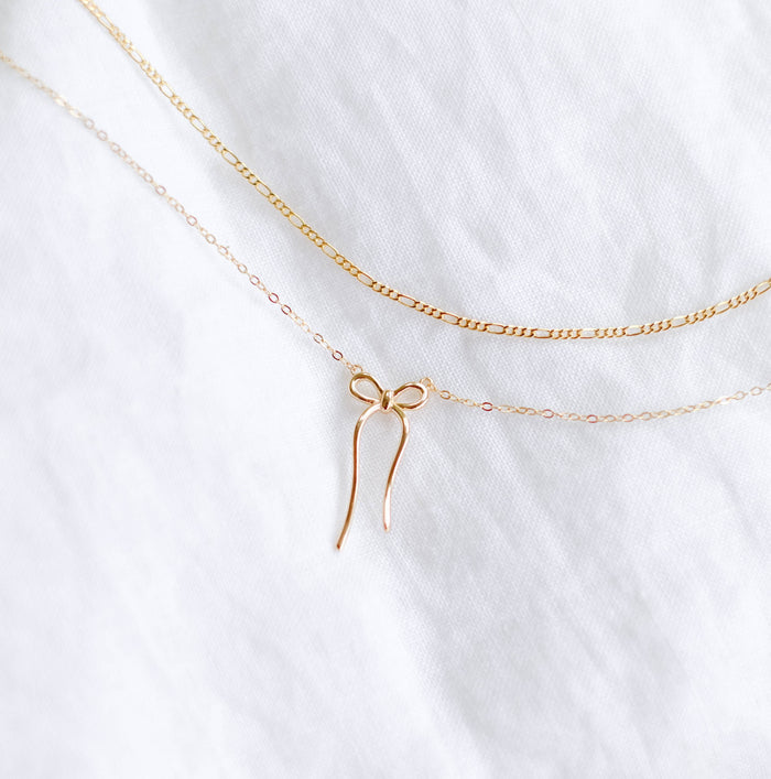 The Bow Daily Set by LLUME Jewelry features two delicate gold necklaces: a classic chain and the Colette Necklace with a charming bow pendant—perfect for graceful, effortless layering.