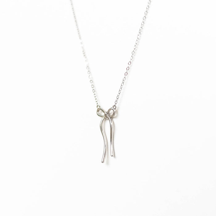The LLUME Jewelry Bow Necklace is a delicate silver chain with a minimalist bow pendant, shown on a plain white background. This limited edition piece brings subtle elegance to any outfit.