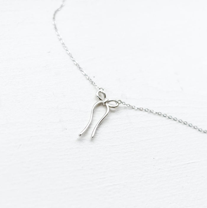 The LLUME Jewelry Bow Necklace is a limited edition silver piece with a minimalist bow-shaped pendant, elegantly displayed on a white background.