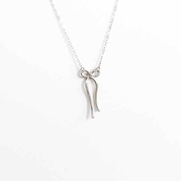 The LLUME Jewelry Bow Necklace is a delicate gold-plated piece featuring a pendant shaped like a minimalist bow, shown against a plain white background.