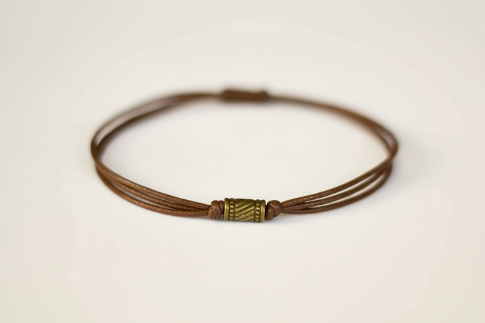 Brown leather cord bracelet with a metal clasp on a light beige background