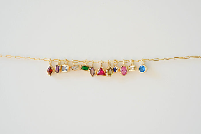 The LLUME Jewelry Build a Birthstone Necklace features a gold chain with colorful, gold-plated charms in oval, round, square, and rectangular gemstone shapes, shown on a white background.