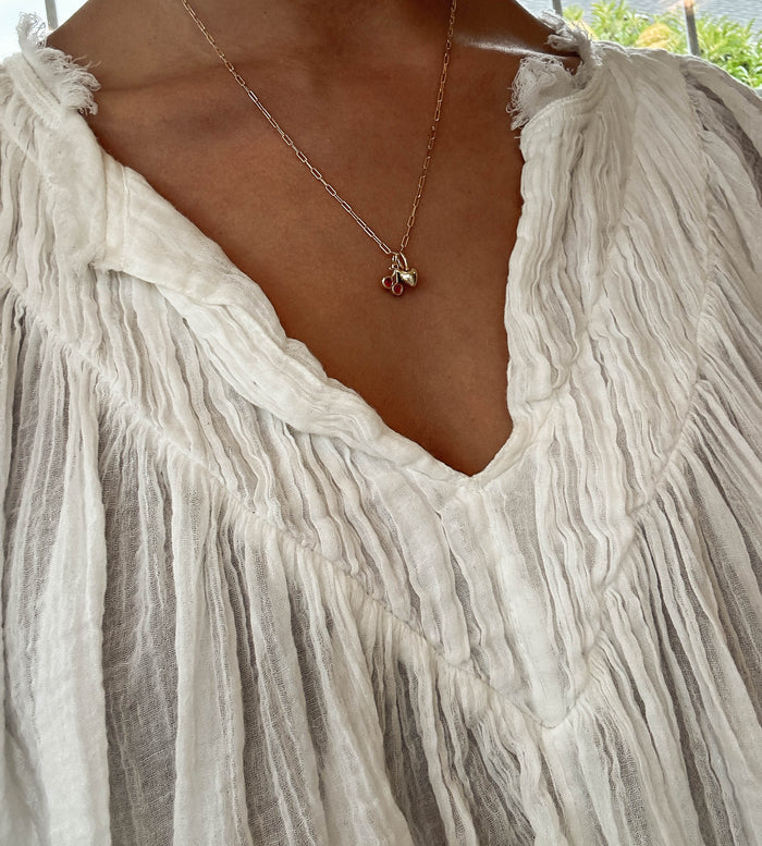 A close-up of a person wearing a textured white v-neck blouse and the LLUME Jewelry Build a Charm Necklace with delicate gold filled cherry-shaped charms.