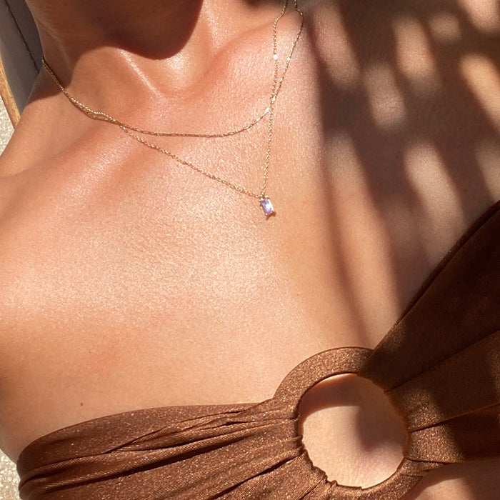 A close-up of someone wearing a brown, shimmery cut-out top and the LLUME Jewelry Celia Golden Set, with sunlight highlighting the layered necklaces and their circular ring detail beautifully.