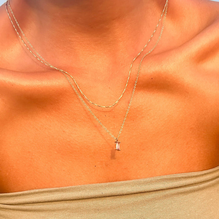 A person wearing the Celia Golden Set by LLUME Jewelry, a delicate gold necklace duo with a petite pendant, shines against sun-kissed skin and an off-shoulder olive green top.