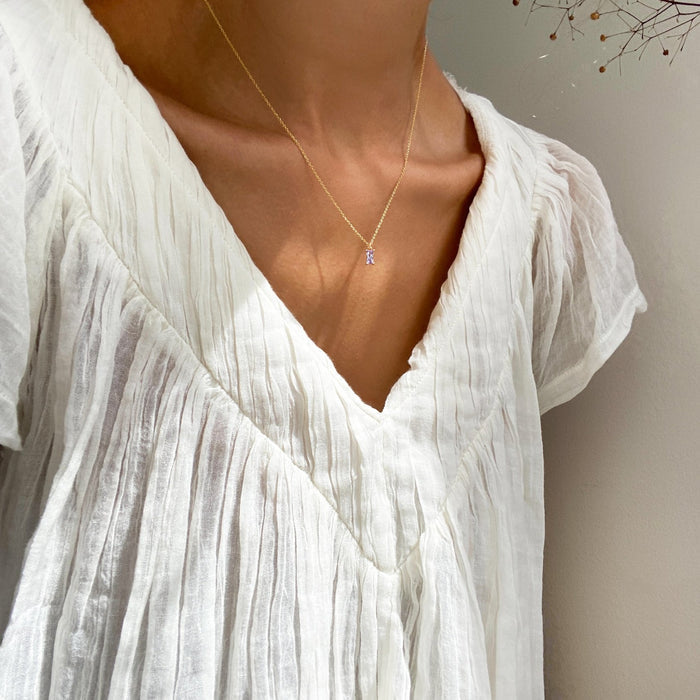 A person wears a white, pleated V-neck blouse and LLUME Jewelry’s Celia Necklace; soft light enhances the fabric’s texture and the wearer’s collarbones.