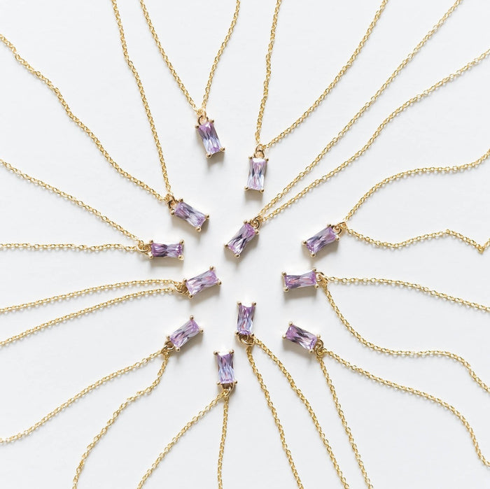 Ten Celia Necklaces by LLUME Jewelry, each a gold vermeil piece with a rectangular lilac gemstone pendant, are arranged in a circle on a white background, radiating outward like sunrays.