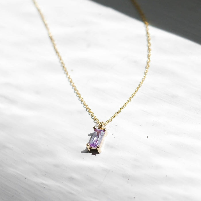 The Celia Necklace by LLUME Jewelry is a delicate gold vermeil piece featuring a small rectangular lilac gemstone pendant, displayed on a white textured surface in natural light.