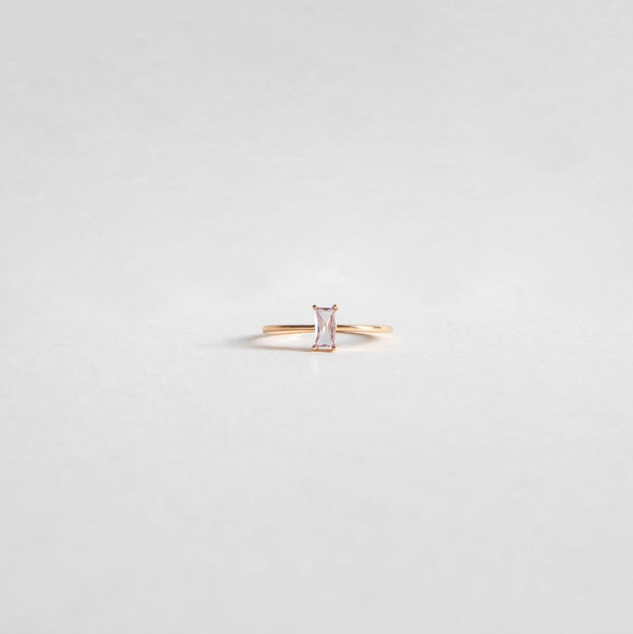 The Celia Ring by LLUME Jewelry features a vertical rectangular light pink gemstone set on a delicate gold-filled band, perfect for stacking. Shown against a plain white background.