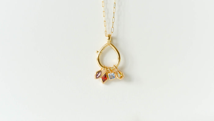 The LLUME Jewelry Charm Holder is a gold necklace with a teardrop-shaped pendant and four colorful gemstone charms in pink, red, blue, and yellow, crafted with 18K gold-filled accents and shown on a plain white background.