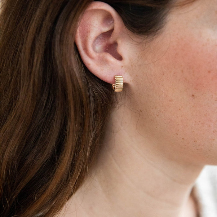Close-up of a woman’s ear with long brown hair wearing Chloe Hoops by LLUME Jewelry. The light skin tone highlights the ridged, 18k gold plated design for a minimal, timeless look.