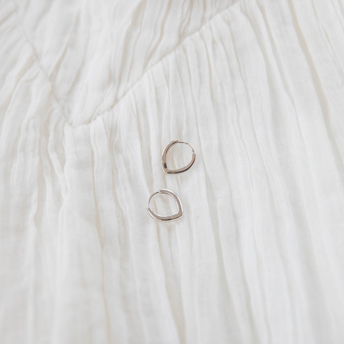 Two Classic Pointed Hoop Silver earrings by LLUME Jewelry, crafted in 925 silver with an irregular shape, rest on a softly textured white crinkled fabric background.