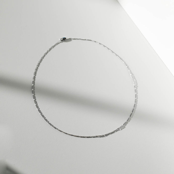 The Colette Necklace Silver by LLUME Jewelry, crafted from sterling silver, is arranged in an oval on a smooth, light surface with soft shadows—a versatile and elegant accessory.