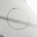 The Colette Necklace Silver by LLUME Jewelry, crafted from sterling silver, is arranged in an oval on a smooth, light surface with soft shadows—a versatile and elegant accessory.