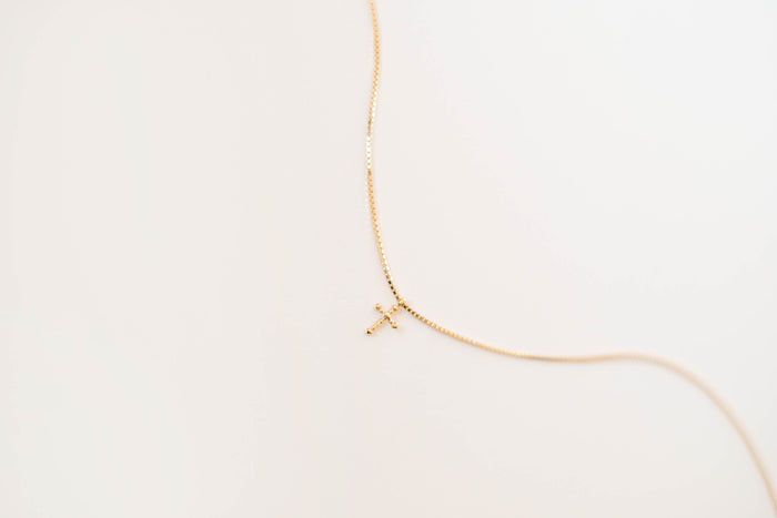 The LLUME Jewelry Cross Necklace showcases a dainty gold-plated chain with a cross pendant, elegantly displayed against a simple light background.