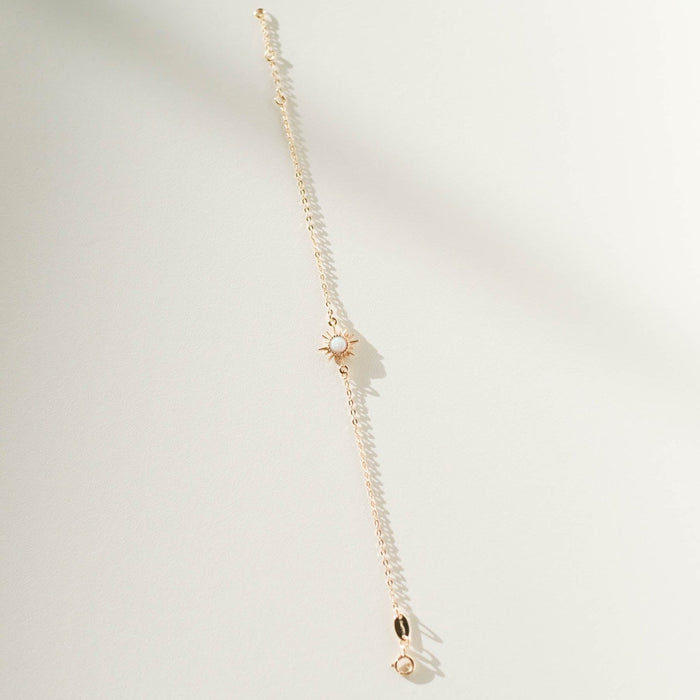 The Cyra Bracelet by LLUME Jewelry is a gold-plated sterling silver piece with a sun-shaped charm and a central white stone, elegantly displayed on a light textured surface with soft shadows.