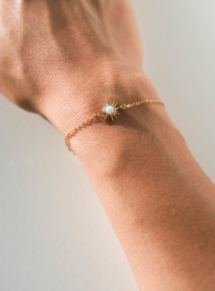 The Cyra Bracelet by LLUME Jewelry, a gold plated sterling silver piece with an adjustable opal charm, is shown on a wrist against a light background.