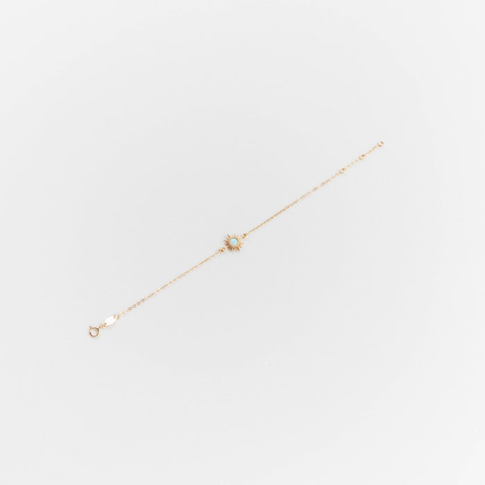 The Cyra Bracelet by LLUME Jewelry is a gold plated sterling silver piece featuring a small opal sun charm with a white center, displayed elegantly on a white background.