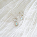 Cyra Hoops Silver by LLUME Jewelry: 925 silver hoop earrings with sunburst pendants and light blue stones, displayed on a softly textured white fabric background.