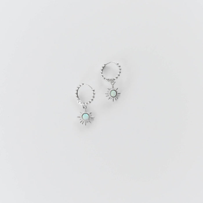 The Cyra Hoops Silver by LLUME Jewelry are 925 silver hoop earrings with sun-shaped charms, each featuring a light blue opal center, shown on a plain white background.