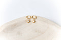The Cyra Hoops by LLUME Jewelry are gold-plated sterling silver earrings with sun-shaped pendants and white center stones, shown on a light wooden dish against a white background.