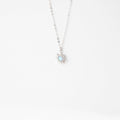 The Cyra Necklace Silver by LLUME Jewelry features a delicate 925 sterling silver chain and a small sun-shaped pendant with a light blue gemstone, shown on a plain white background.