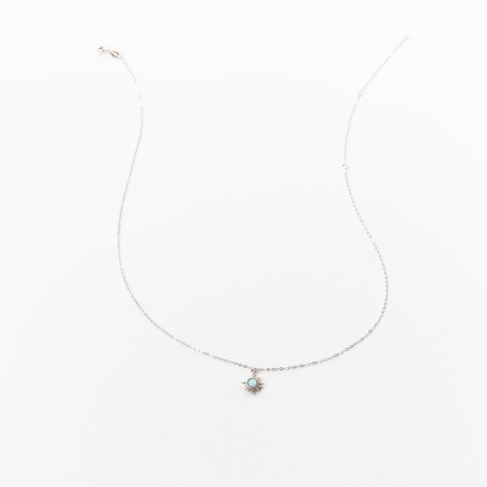 The Cyra Necklace Silver by LLUME Jewelry features a delicate 925 sterling silver chain with a small sun-shaped opal-like pendant, shown on a plain white background.