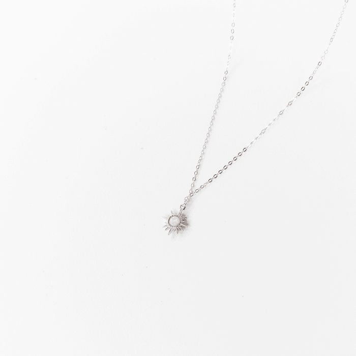 The Cyra Necklace Silver by LLUME Jewelry showcases a delicate layered design with a silver sun-shaped pendant and a small square white opal charm on a 925 sterling silver chain, presented on a plain white backdrop.
