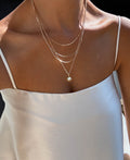 Wearing a white satin camisole, she pairs her look with LLUME Jewelry’s Cyra Solstice Set—a gold layered necklace featuring a radiant opal sun pendant that shimmers beautifully in the natural light.