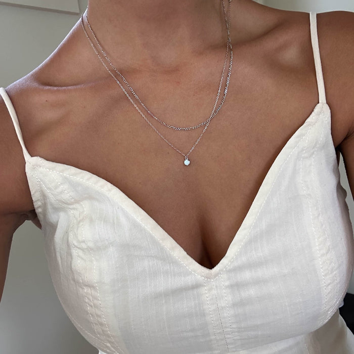 A person wears a white spaghetti-strap V-neck top and two delicate silver pieces from LLUME Jewelry—the Daily Set Silver. The cropped photo highlights only the neck and upper chest.